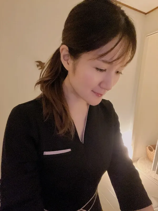 Professional therapist in black spa uniform with welcoming presence in a calm spa setting.